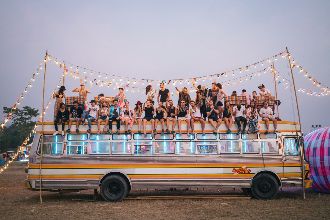 Festival-goers standing and sitting on top of a decorated bus with string lights at Wonderfruit festival in Thailand.