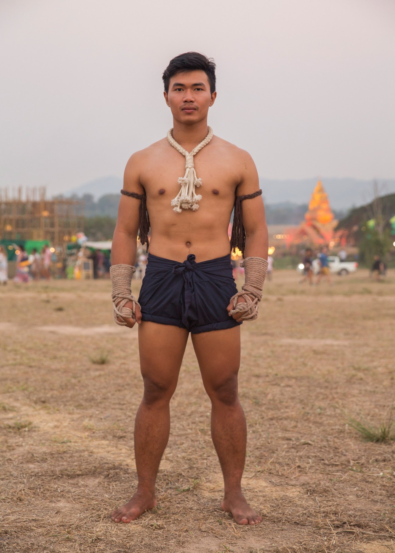 Shirtless man wearing traditional Thai-style rope necklace and arm bands at Wonderfruit festival