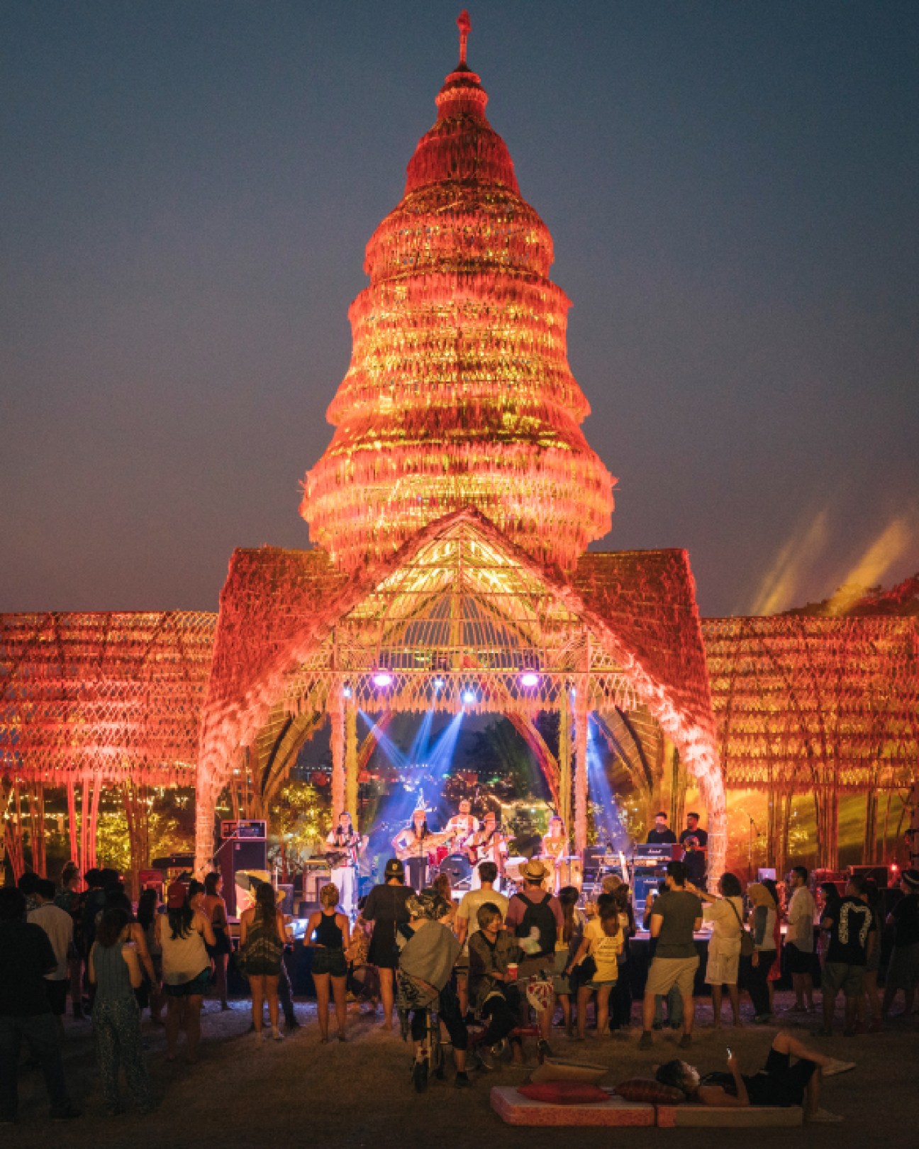 Illuminated rice-made stage shaped like a Thai temple at Wonderfruit festival with band performing and crowd gathered at night.