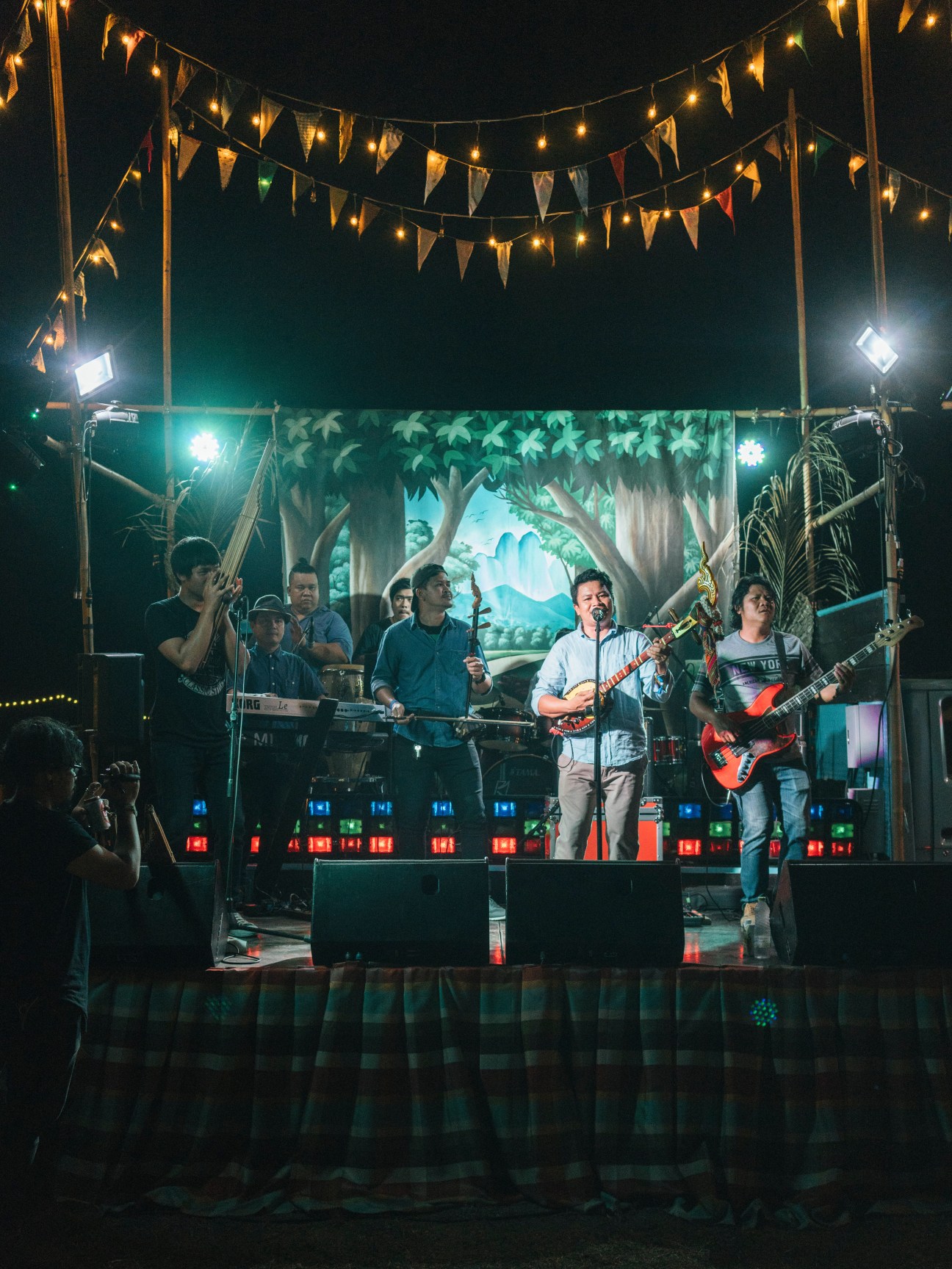 All Thidsa band performs on stage at night with illuminated backdrop and festive bunting overhead.