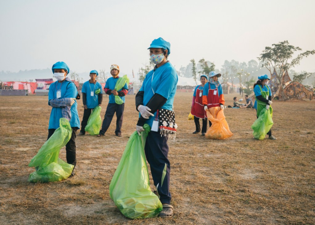 Festival cleanup crew in blue uniforms and masks collecting waste in green bags at Wonderfruit.