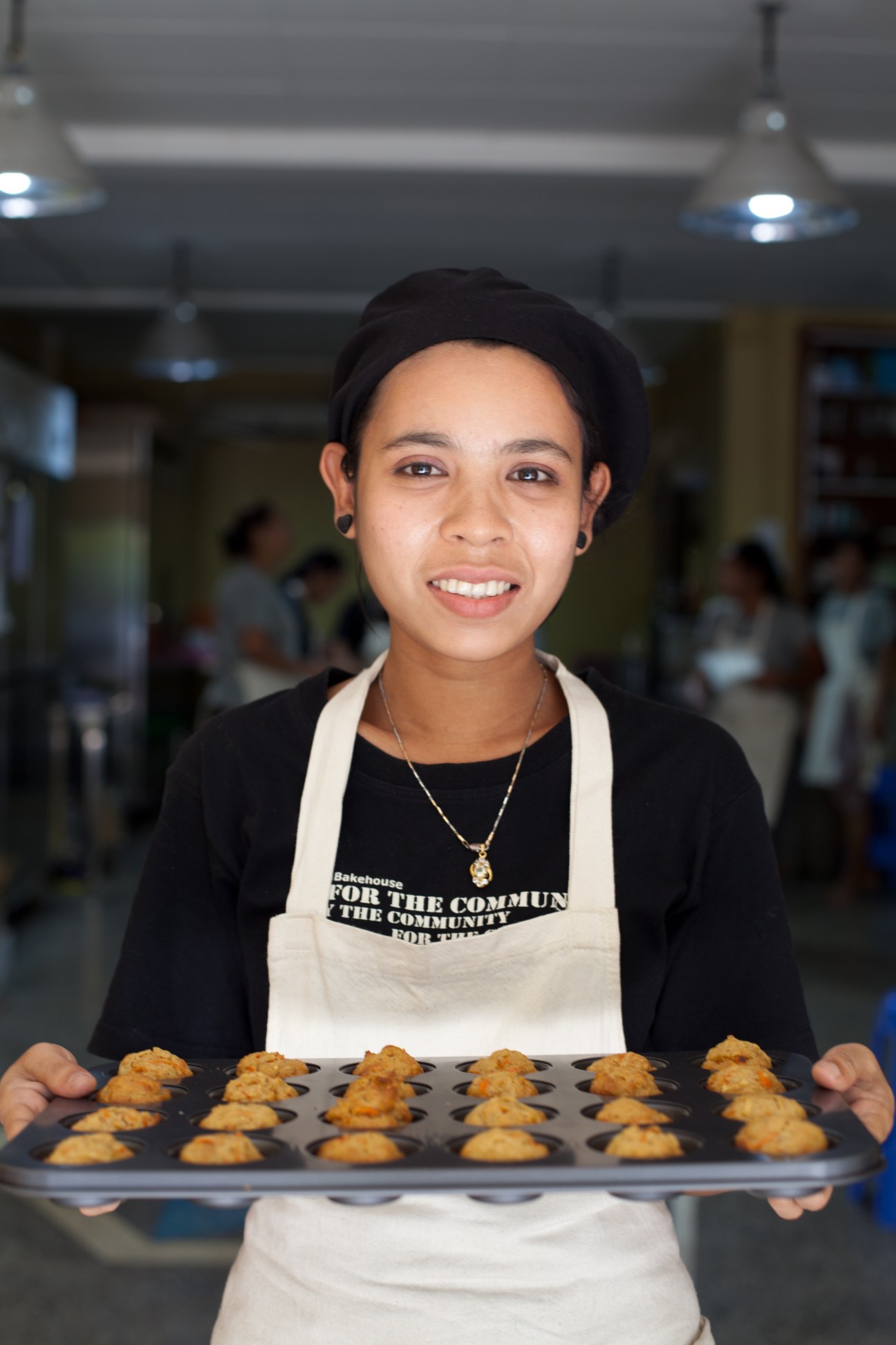 Female baker at Yangon Bakehouse holds tray of freshly baked cookies wearing white apron.