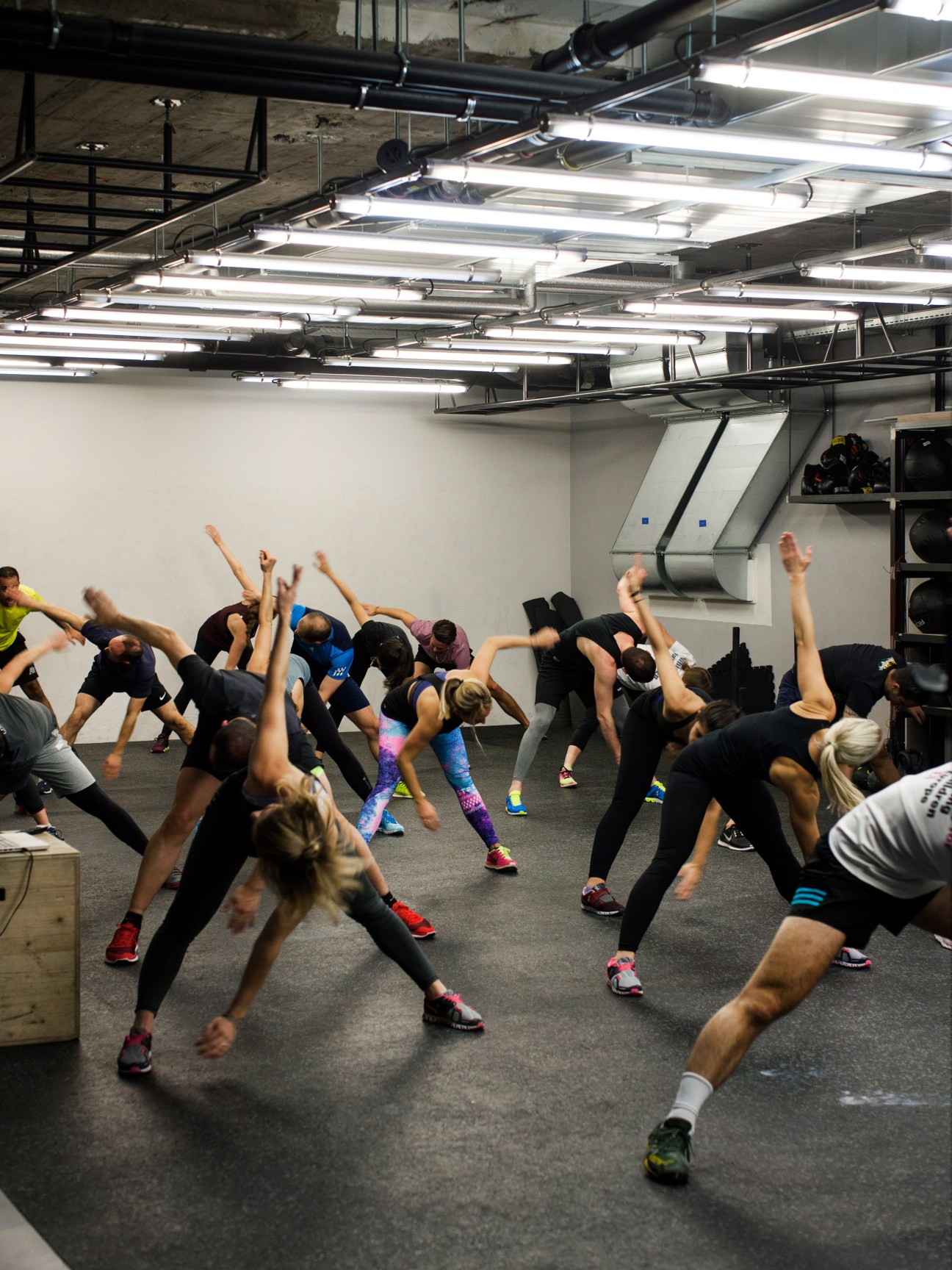 Group fitness class at Balboa Bar & Gym with participants performing synchronized exercises in a modern gym studio with industrial ceiling.