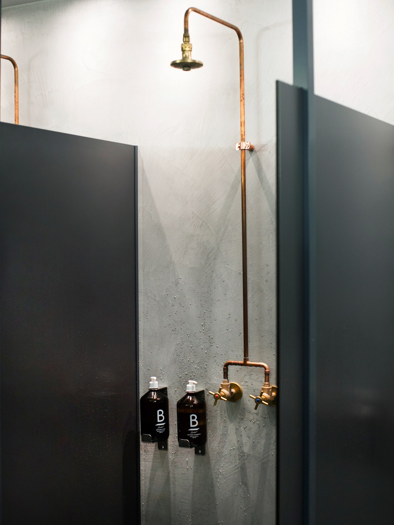 Copper shower fixture with brass showerhead and Soeder soap bottles on concrete wall at Balboa Bar & Gym.