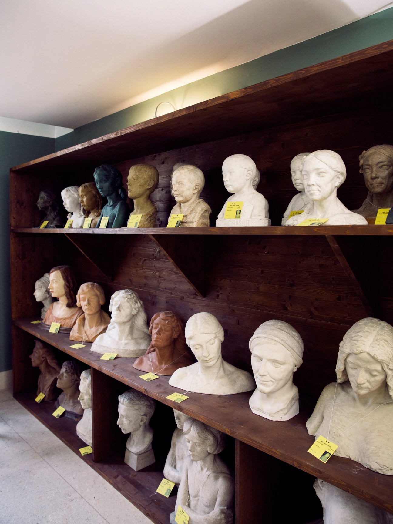 Busts and portrait sculptures displayed on wooden shelves with yellow labels at Museo Revoltella.