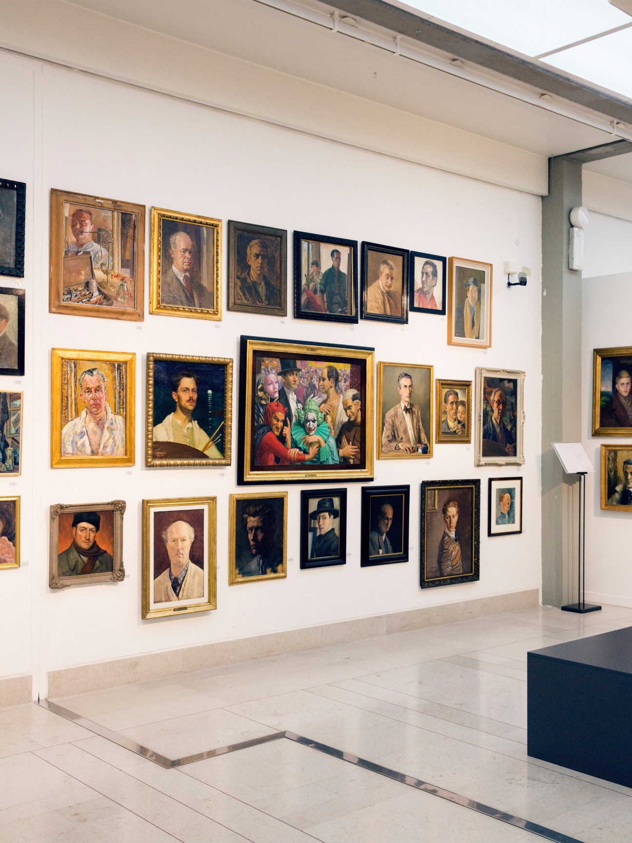 Portrait exhibition gallery at Museo Revoltella with framed paintings in various sizes arranged on white walls.