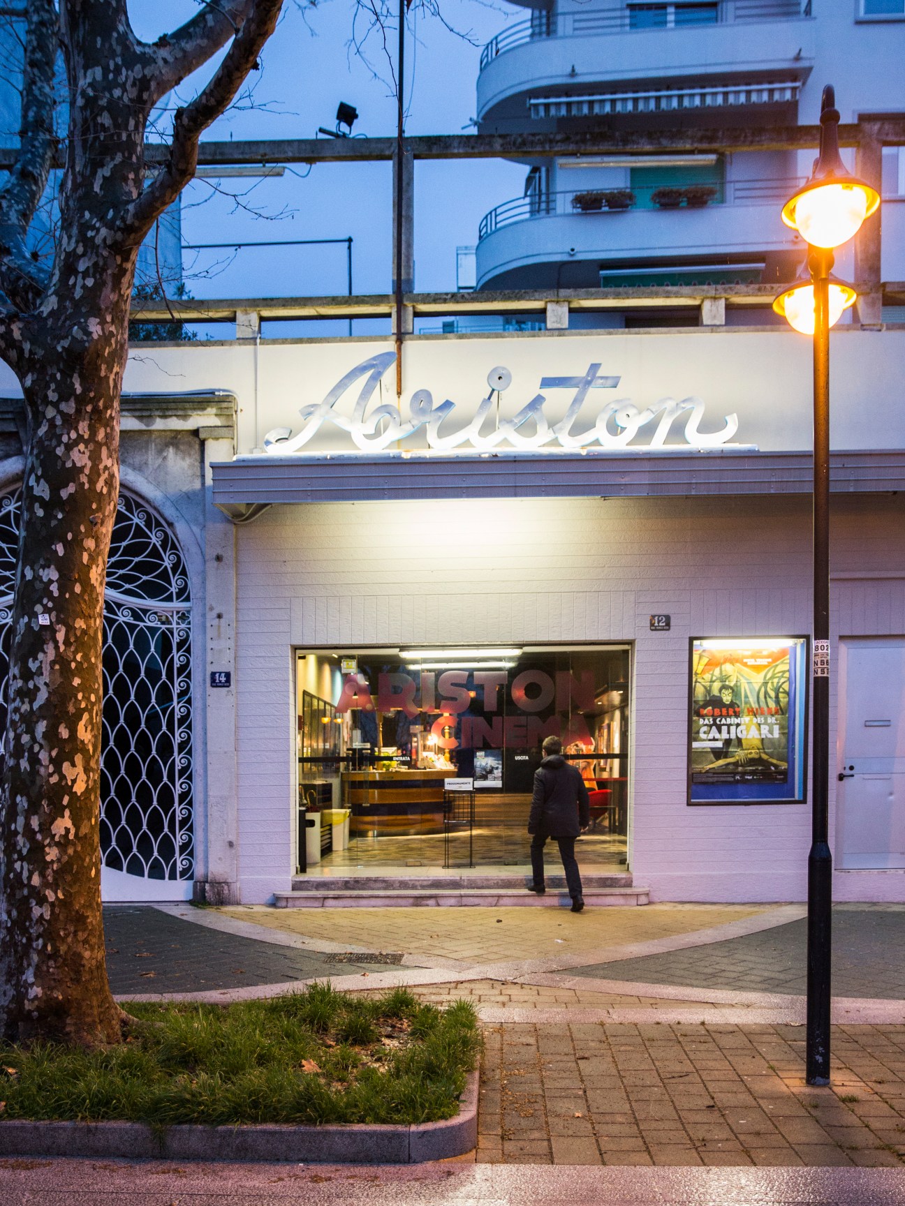 Cinema Ariston entrance at dusk with illuminated signage and a person entering the 1950s-built theatre.