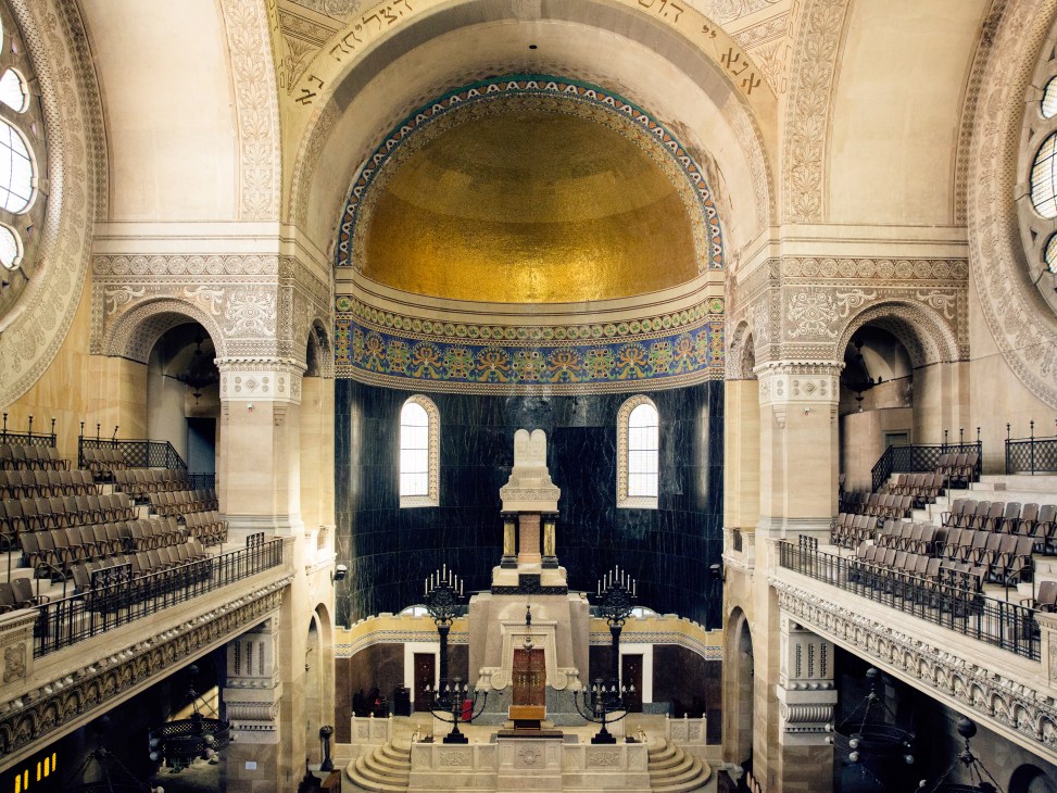 Interior of Trieste Synagogue with golden dome, ornate columns, blue decorative trim and symmetrical seating galleries.