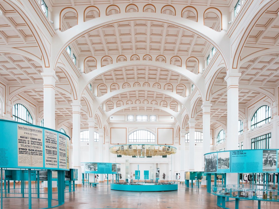 Interior of Salone degli Incanti with arched ceiling, white columns, and turquoise exhibition displays.