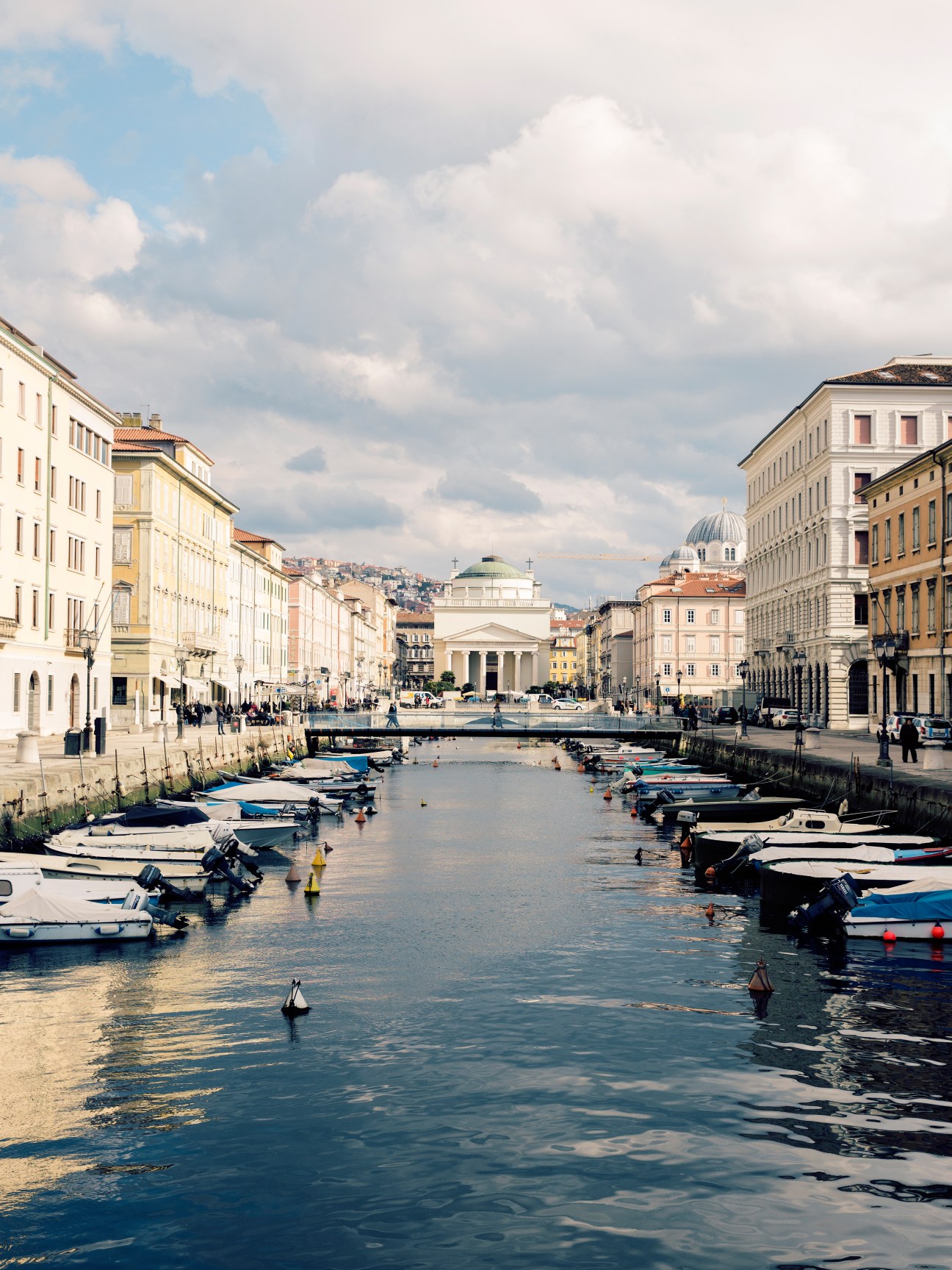 Trieste's Canal Grande with moored boats, Austro-Hungarian architecture, and Sant'Antonio Nuovo church dome in background.