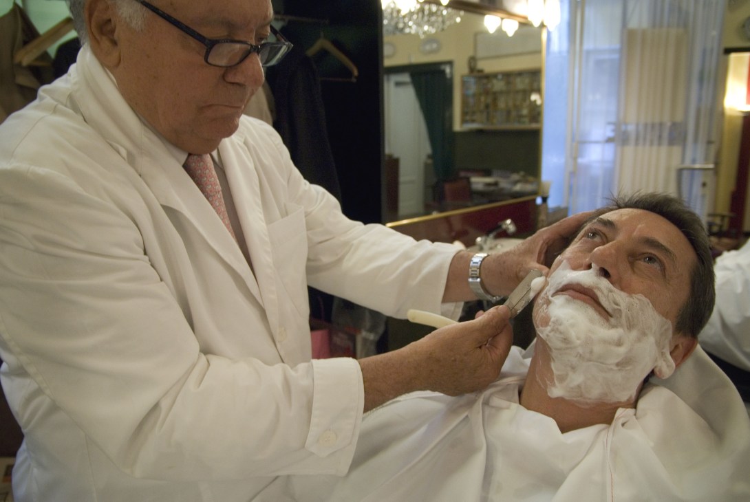 Milan barber Franco Bompieri applying lather and shaving cream to a customer's face in his barbershop.