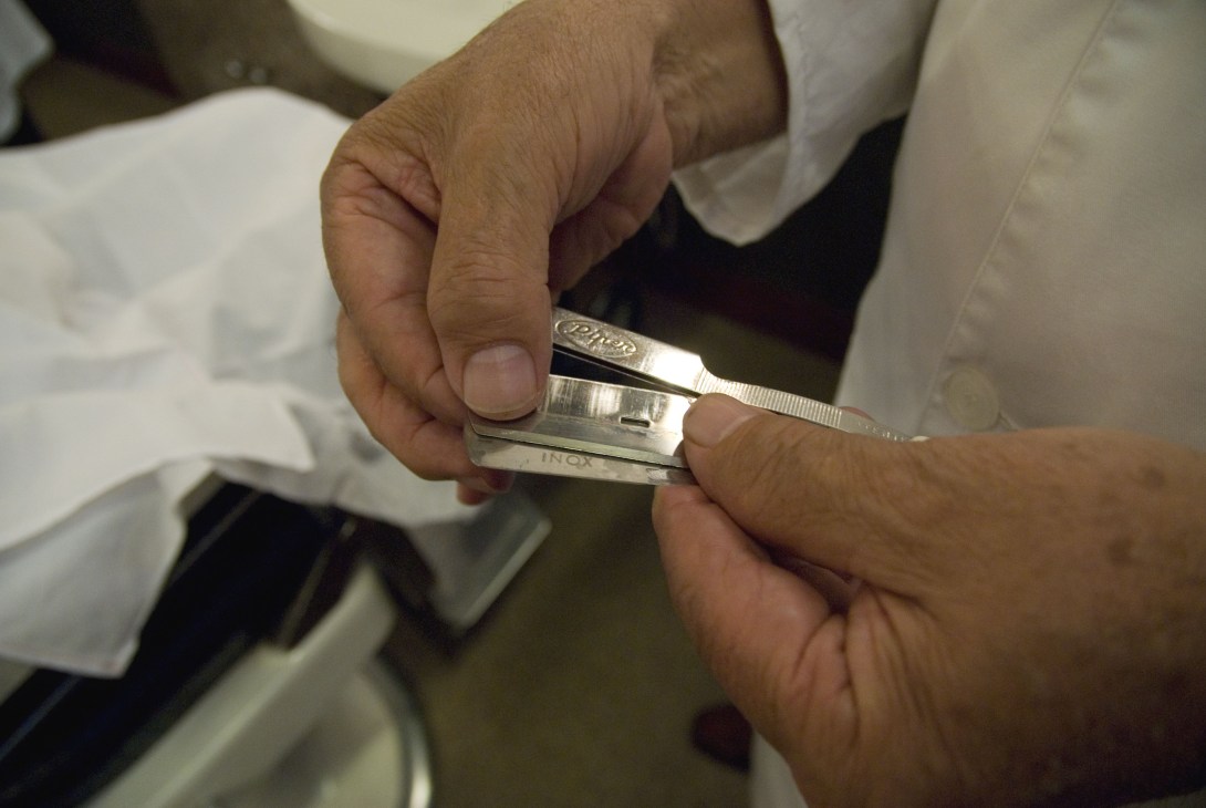 Close-up of hands holding an open straight razor with metal blade and handle marked with text.