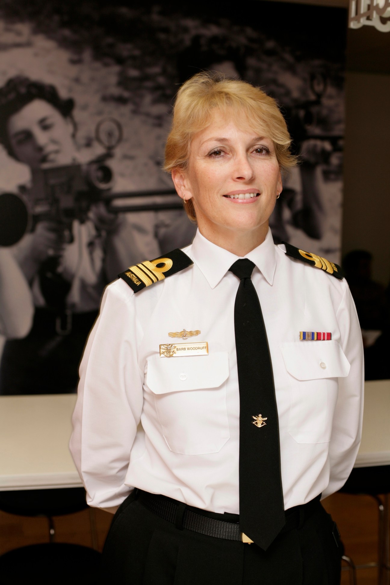 Lieutenant Commander Barb Woodruff in white naval uniform with black tie and shoulder boards.