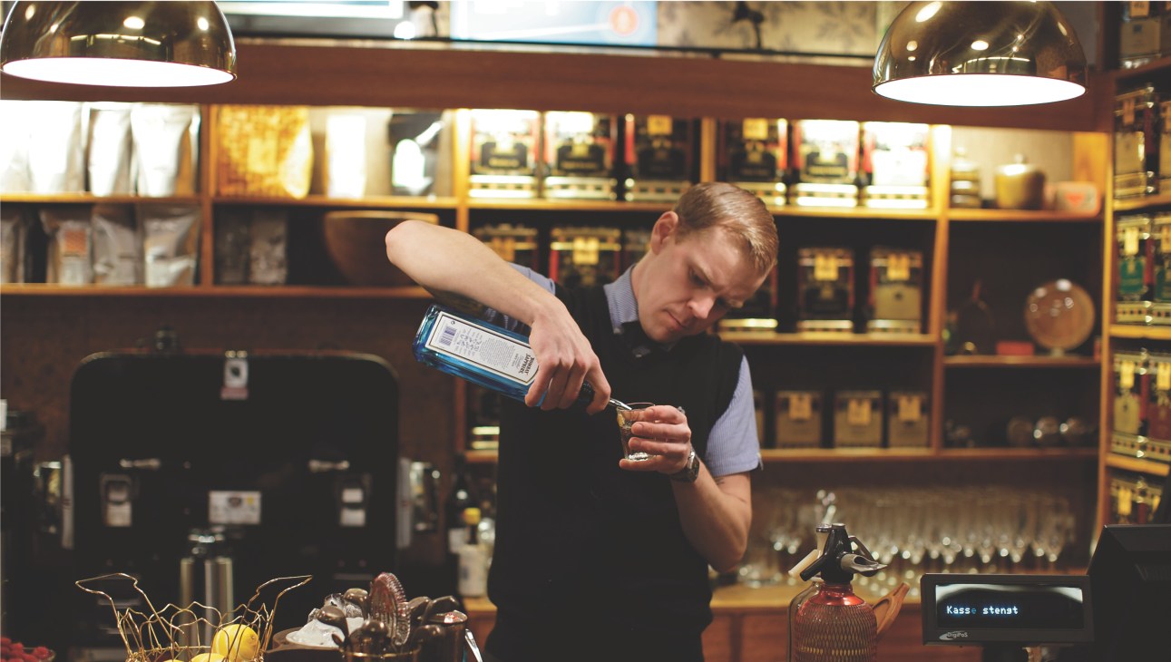 Bartender Halvor Digernes pouring a drink behind a bar with mid-century shelving and lighting.