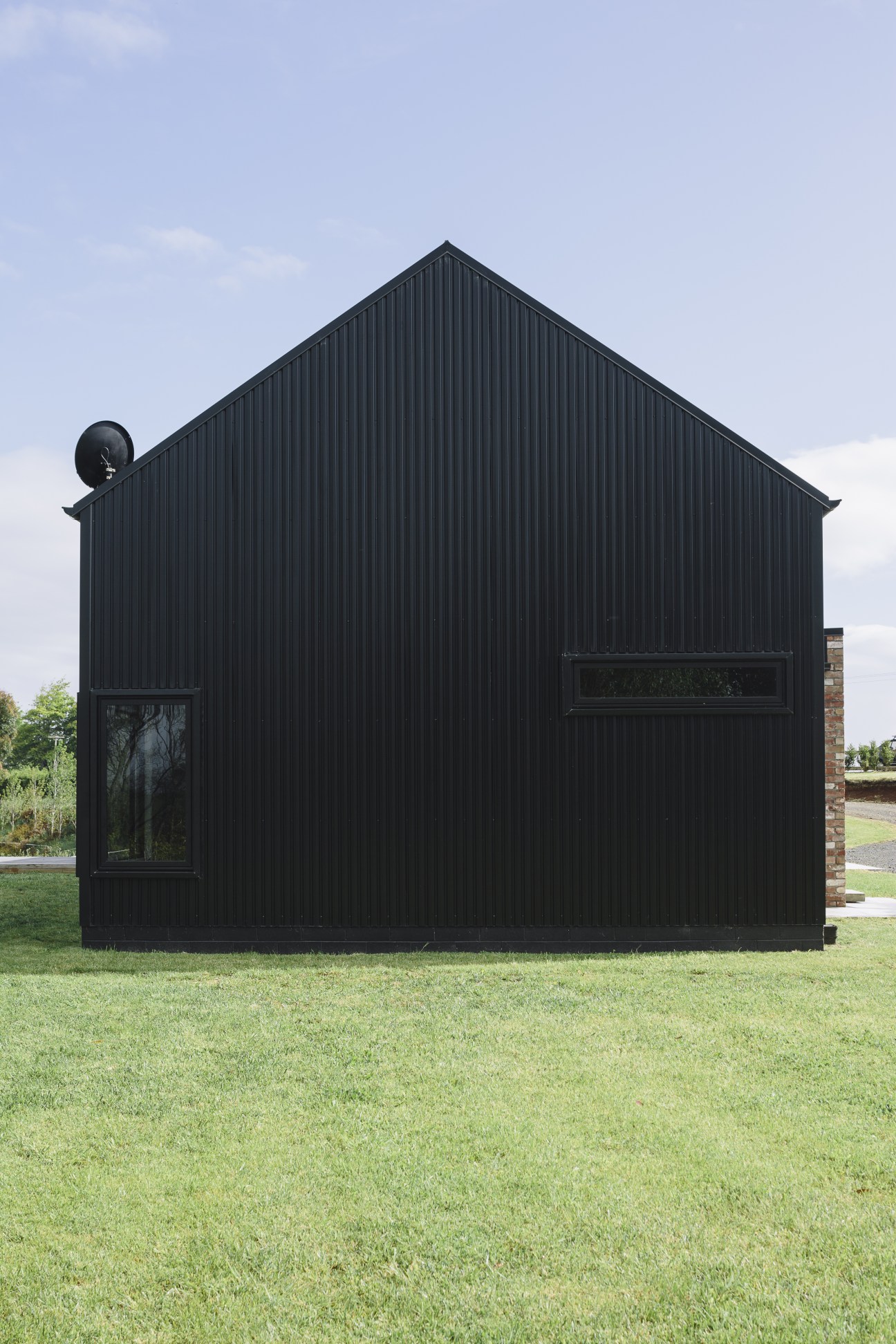 Modern barn-style house with black corrugated steel cladding, pitched roof, and minimal windows set in a rural landscape.