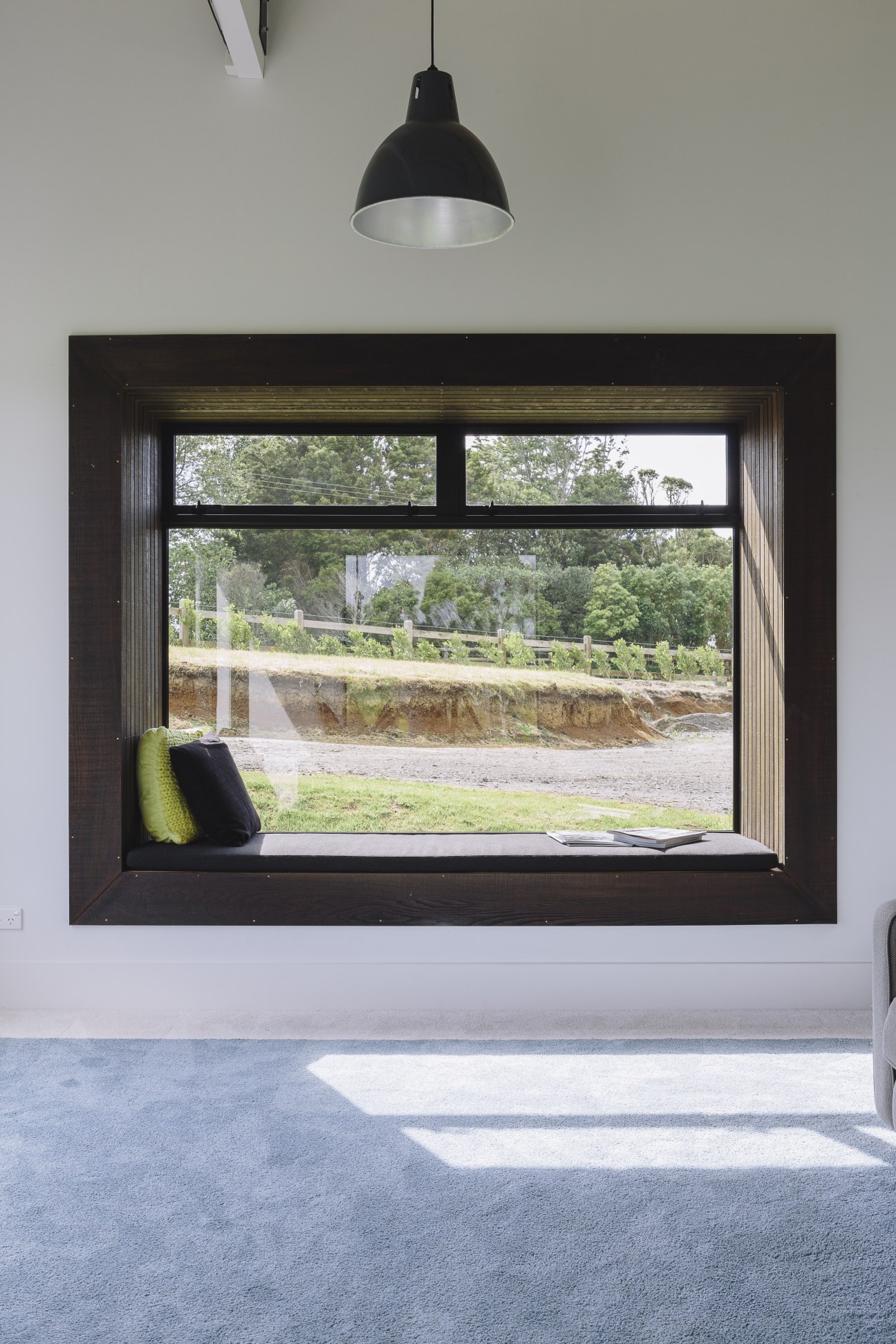Black-framed window seat with cushions overlooking rural New Zealand landscape with fencing and earthworks