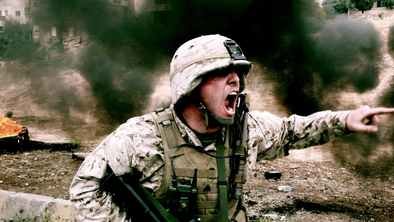 US marine in desert camouflage uniform shouting orders in an urban combat zone.