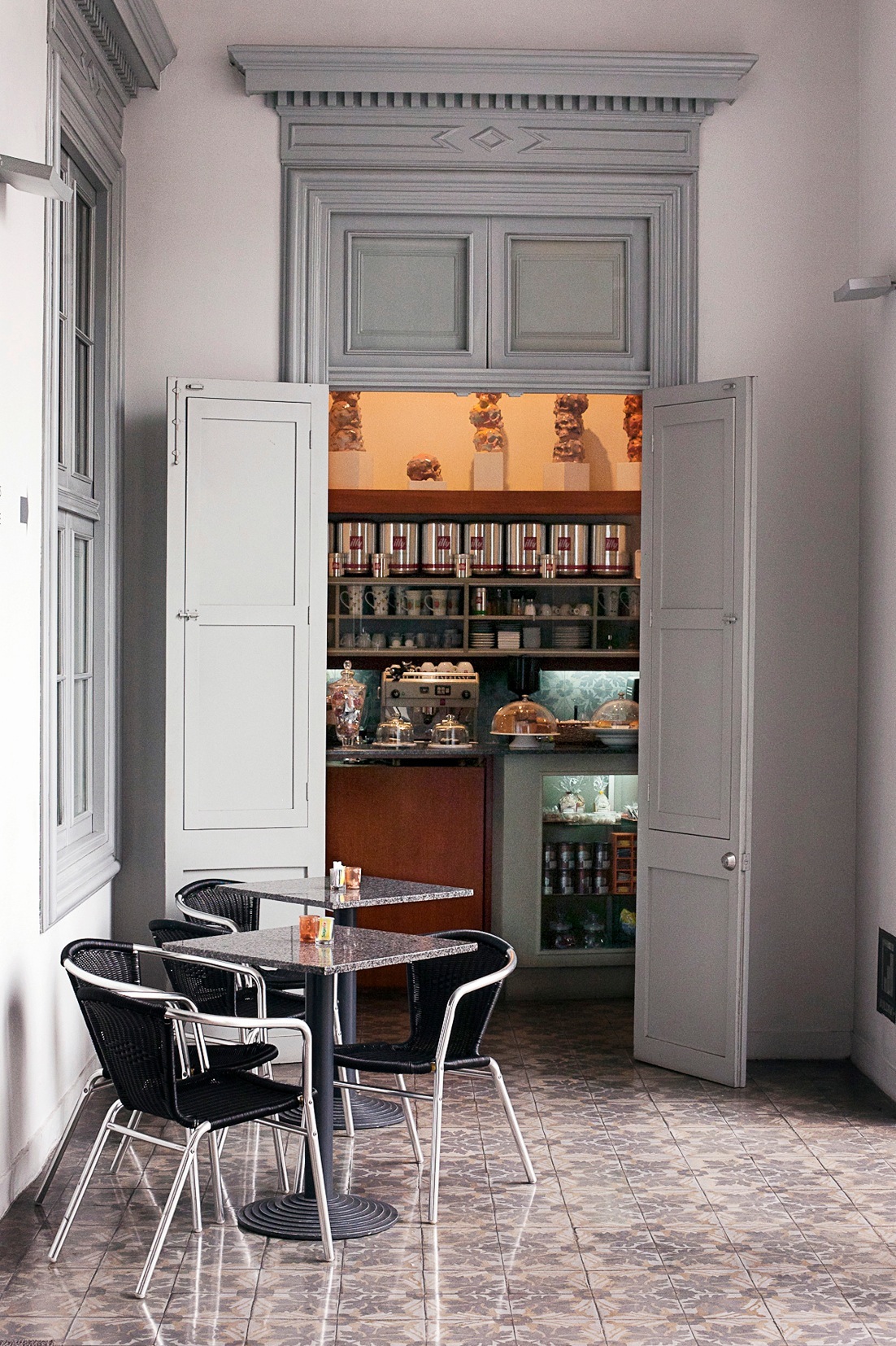 Café seating area at Galería Lucía de la Puente with black chairs, small tables, and built-in shelving displaying art and objects.