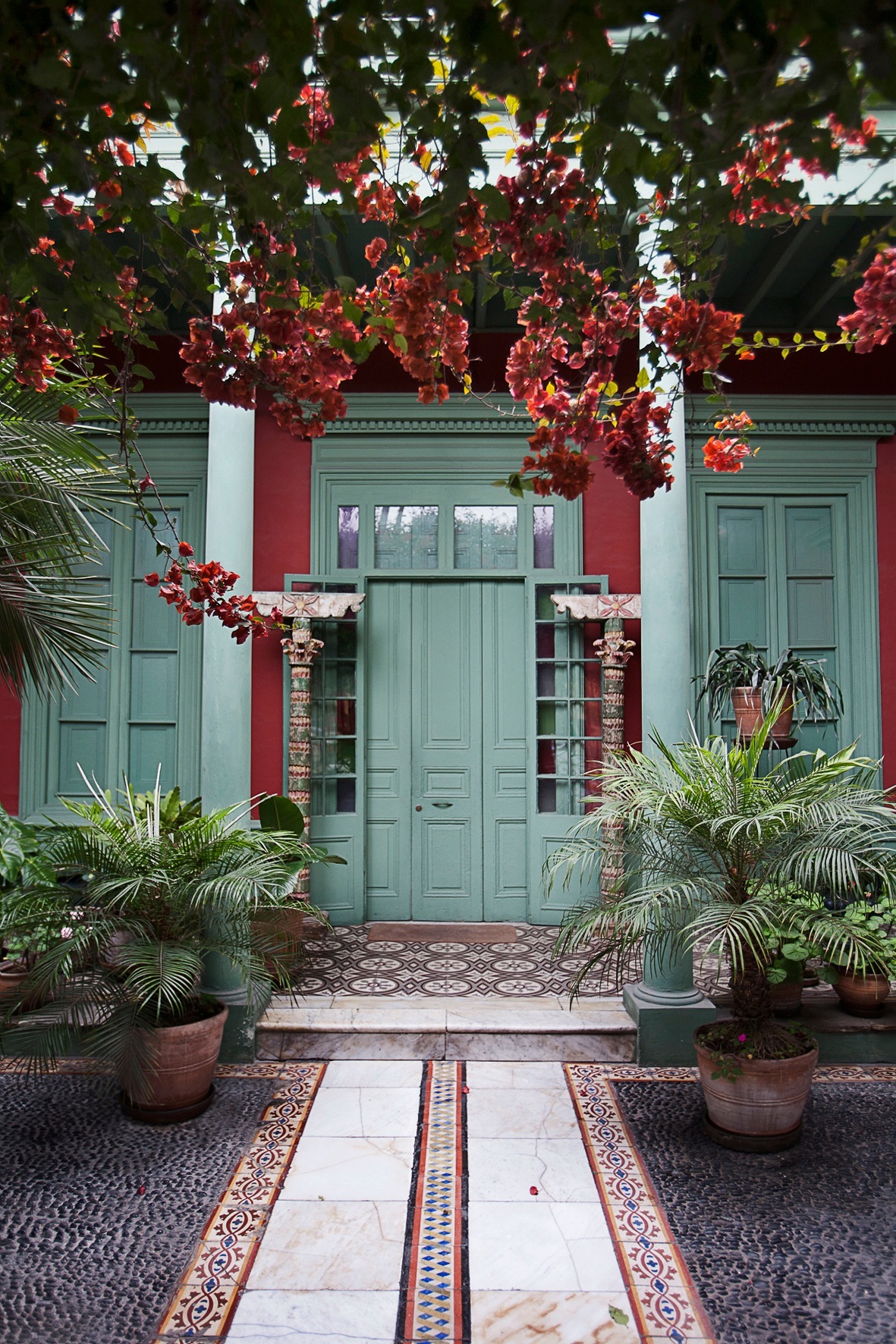 Colonial house courtyard with red bougainvillea flowers, turquoise doors and potted palms in Barranco, Lima.