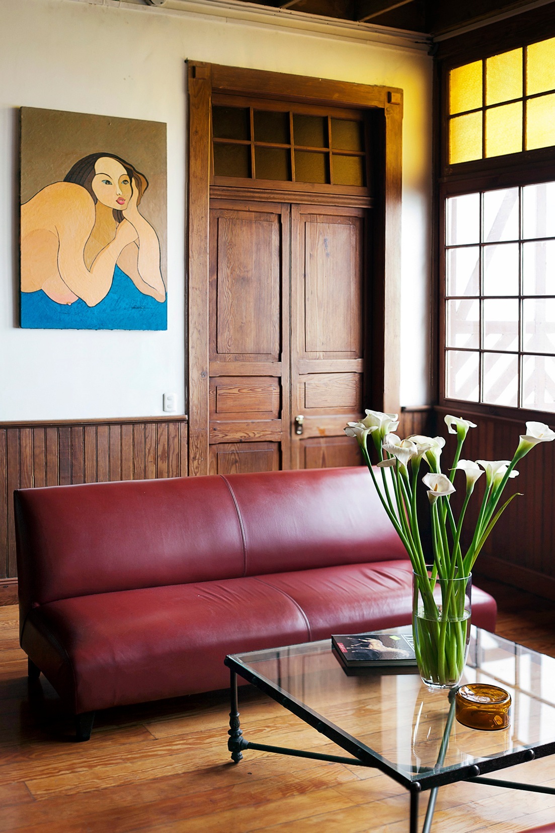 Interior of Second Home Peru hotel showing burgundy leather sofa, wooden doors, and modern artwork.