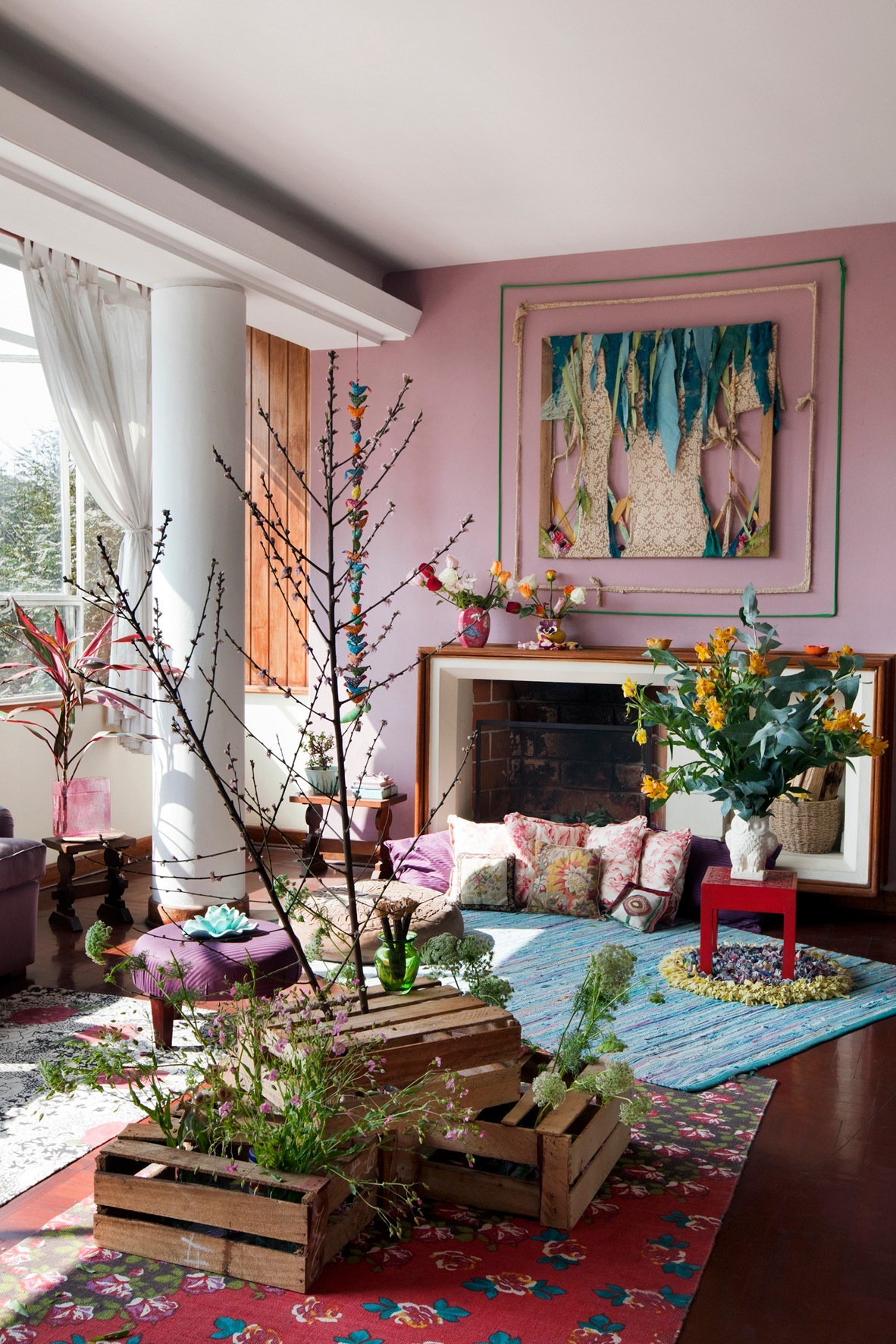 Bright living room with pink walls, fireplace, and colorful artworks and floral arrangements.