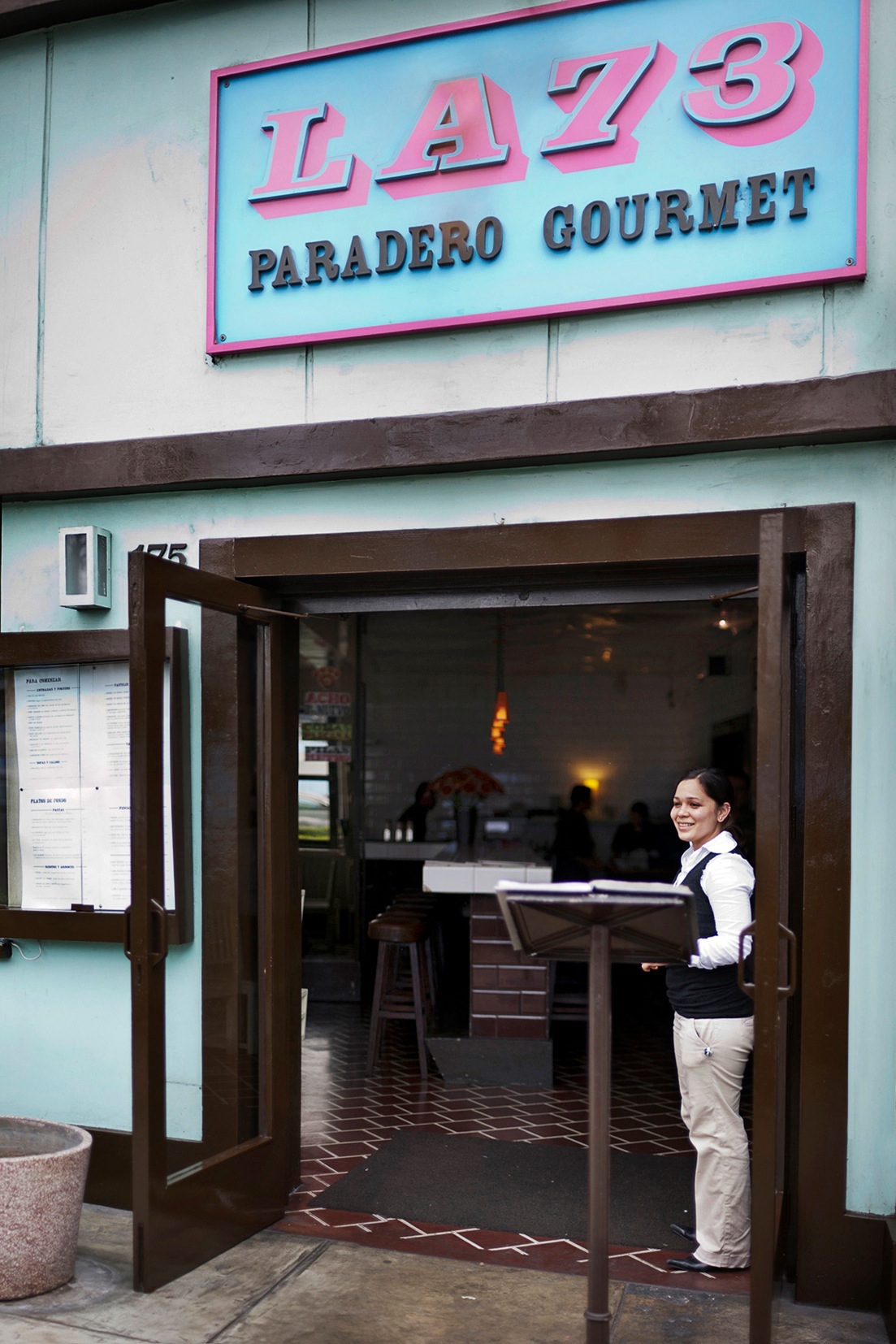 La 73 restaurant exterior with pink and turquoise signage and staff member in doorway.