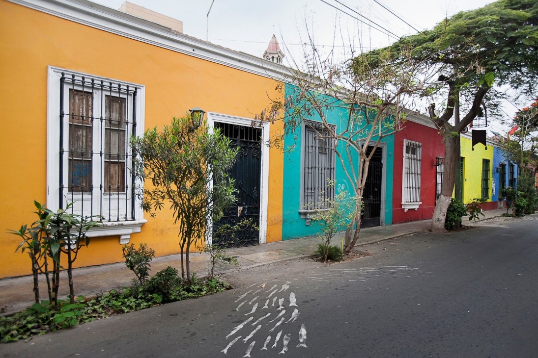 Colorful colonial houses in Barranco with yellow, turquoise, red and lime green facades along a tree-lined street.