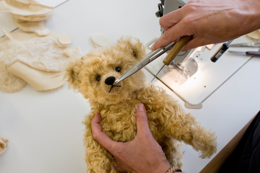 Steiff craftsperson stitching a teddy bear's nose with precision scissors and tools.