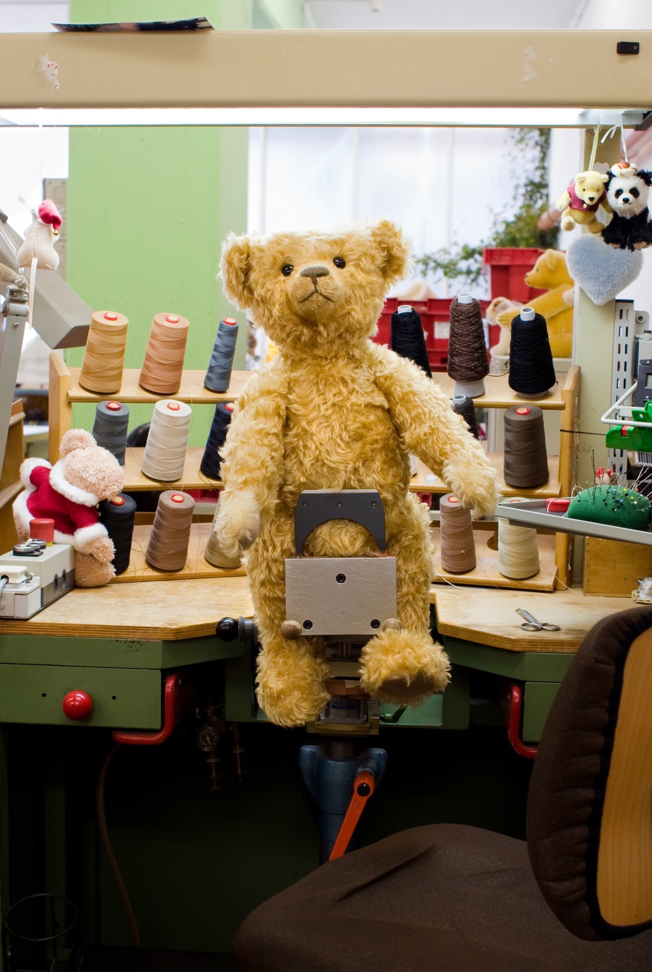 Golden teddy bear positioned at a Steiff workshop sewing station surrounded by spools of thread.