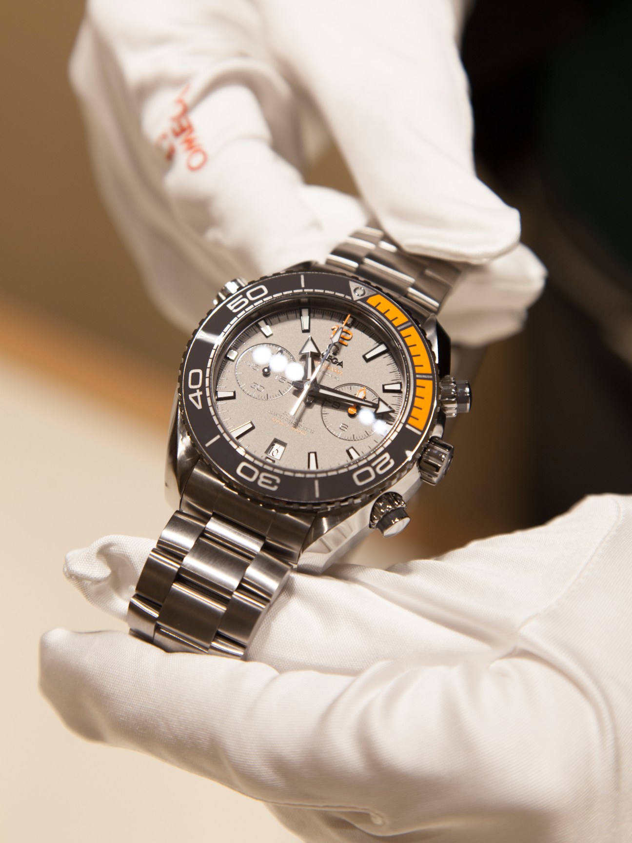 Omega Globemaster watch with silver dial and black bezel held in white-gloved hands.