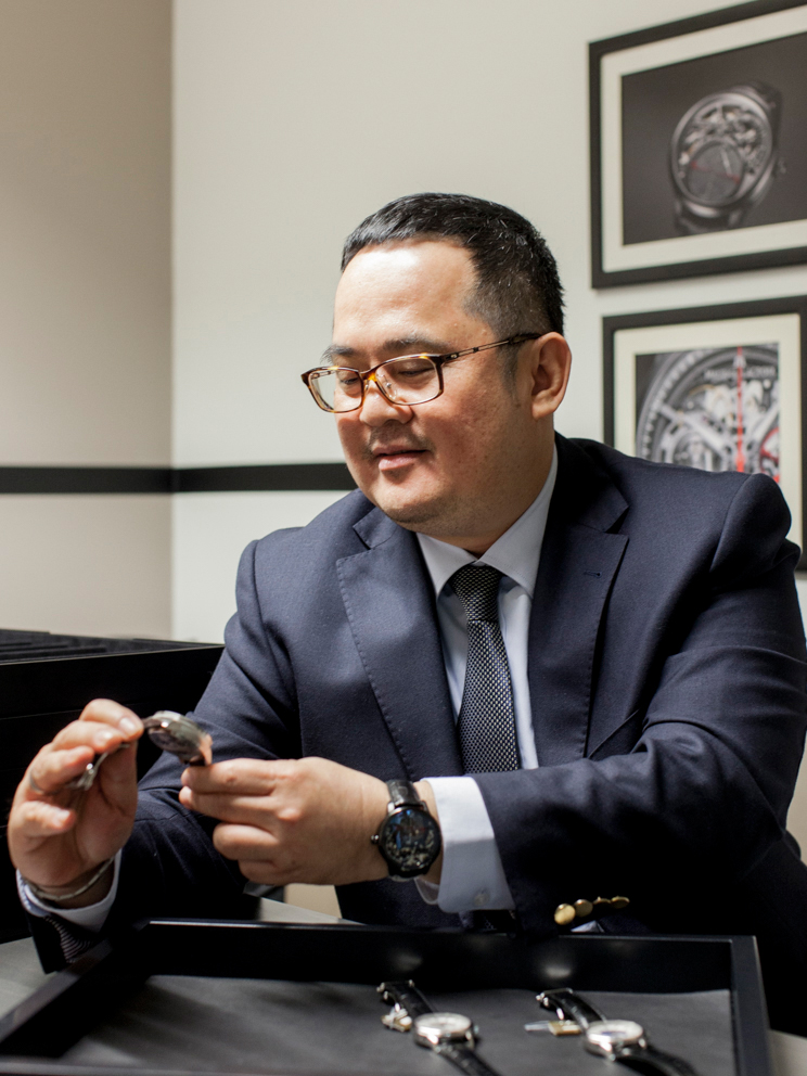 Ong Ban, CEO of Sincere Singapore, examines a watch while seated at a desk.
