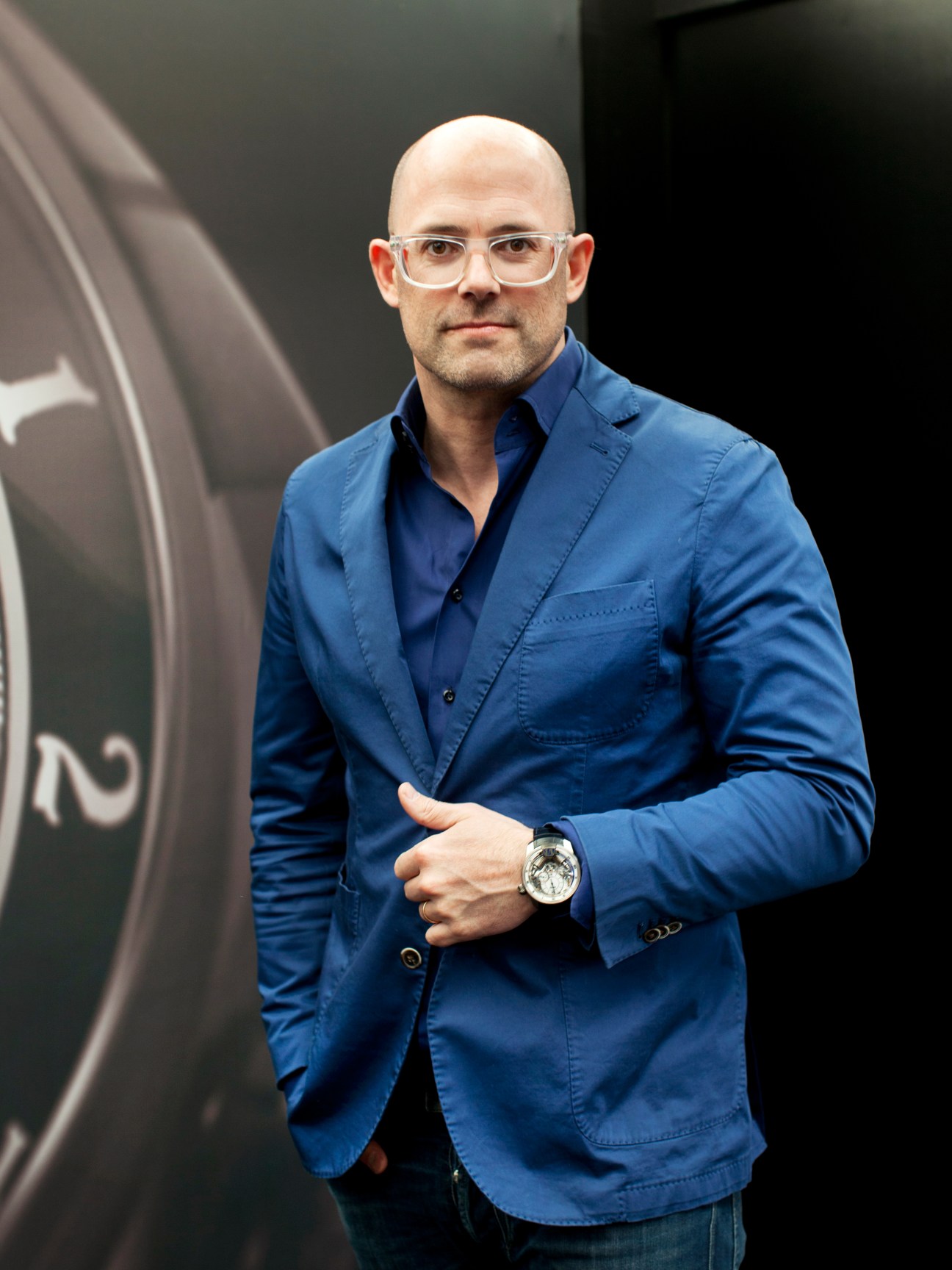 Vincent Perriard, CEO of HYT, wearing a blue shirt and glasses, displays a watch on his wrist.