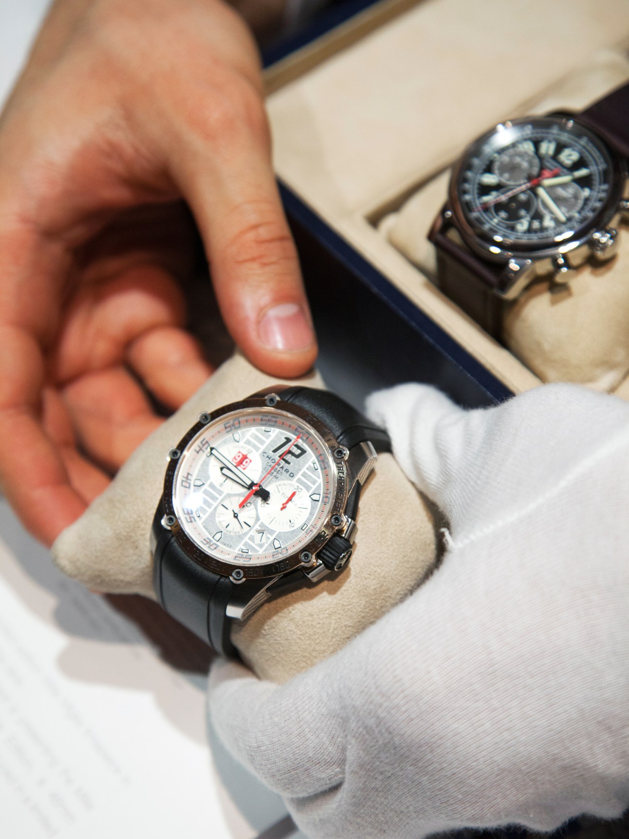 A hand in white gloves displays a Chopard luxury chronograph watch with white dial at Baselworld.