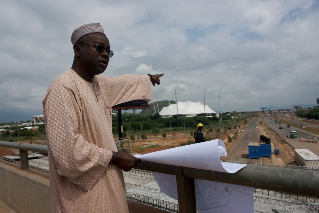 Bashir Haiba, head of Abuja Property Development Agency, holding blueprints while overlooking construction site.