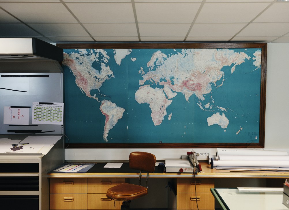 Vintage world map displayed on basement wall above wooden desk with mid-century furniture.