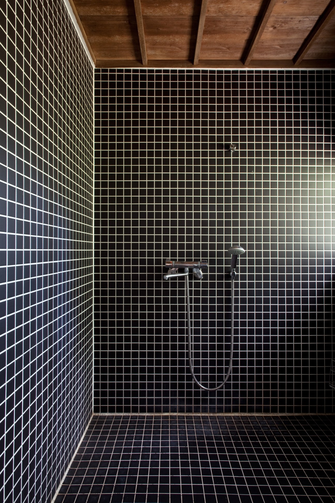 Modern bathroom with black tiled walls and wooden ceiling featuring a wall-mounted shower fixture.