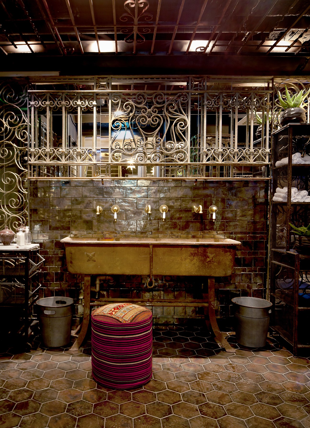Ornate bathroom with vintage brass sink, decorative tilework, and striped pouf seating in Nosh and Chow.
