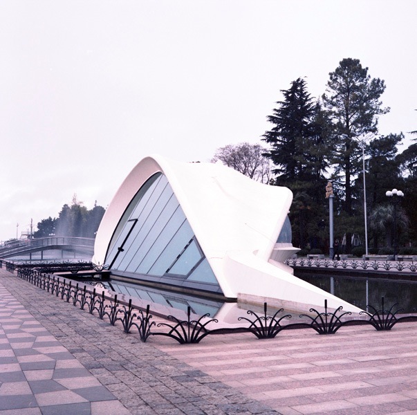 Modern white sculptural structure in Batumi's Seaside Park with patterned pavement and trees.