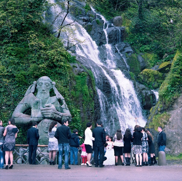 Wedding party gathered in front of a stone statue of St Andrew with a waterfall cascading in the background.