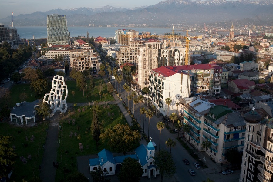 Aerial view of Batumi cityscape with mountains and Black Sea coast visible in background.