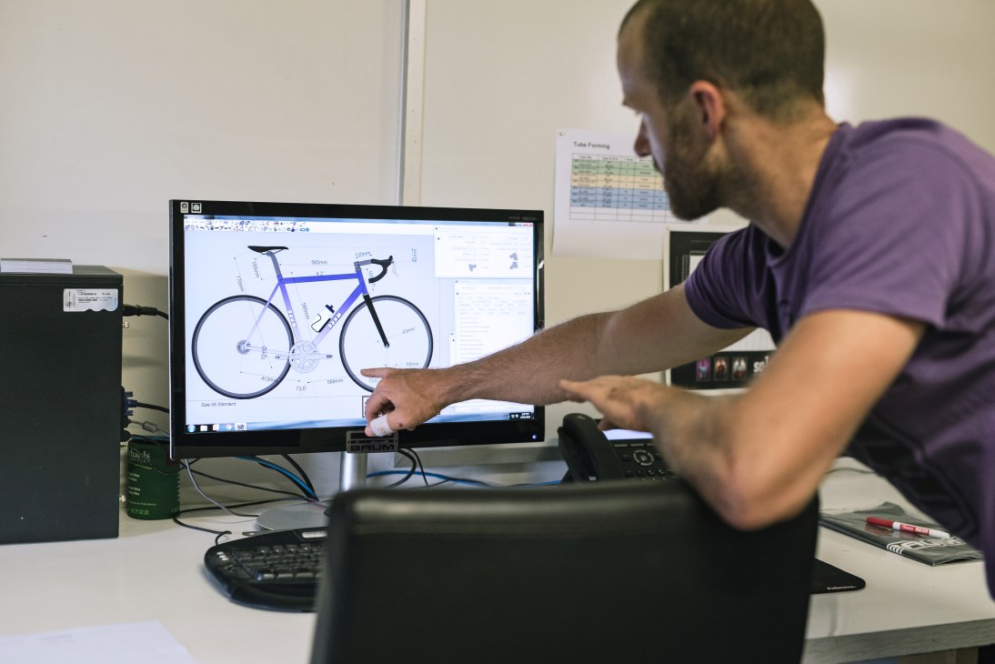 Baum Cycles craftsperson customising a bicycle frame design on computer screen.
