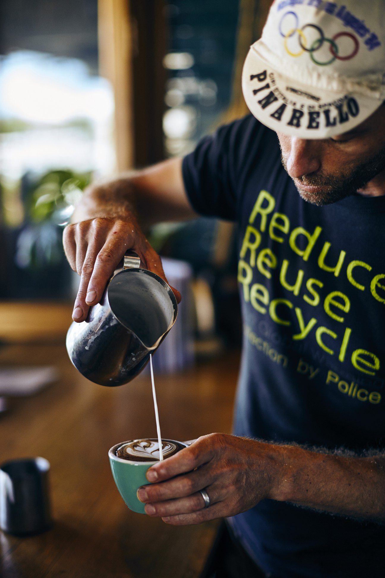 A barista in a Pinabello hat pours latte art into a turquoise cup at the Bayleaf café in Byron Bay.