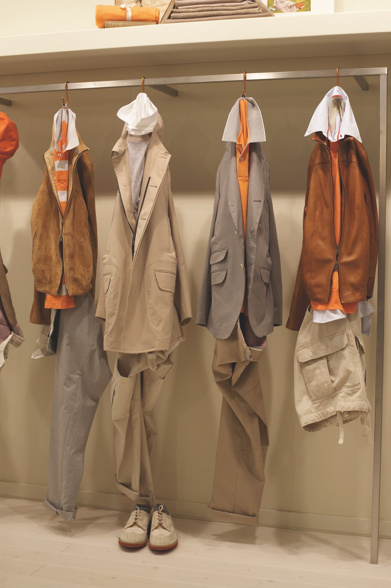 Four mannequins displaying Brunello Cucinelli jackets in neutral tones and burnt orange, with white head coverings and matching orange accents.