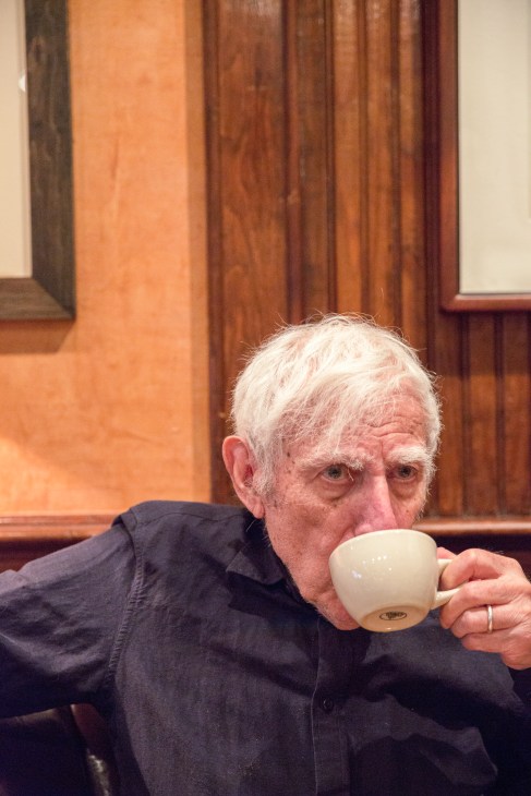 Graphic designer Bob Gill sipping coffee at a restaurant with wood-paneled interior