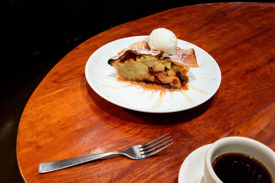 Warm apple and berry pie topped with vanilla ice cream served on a white plate at a wooden table.