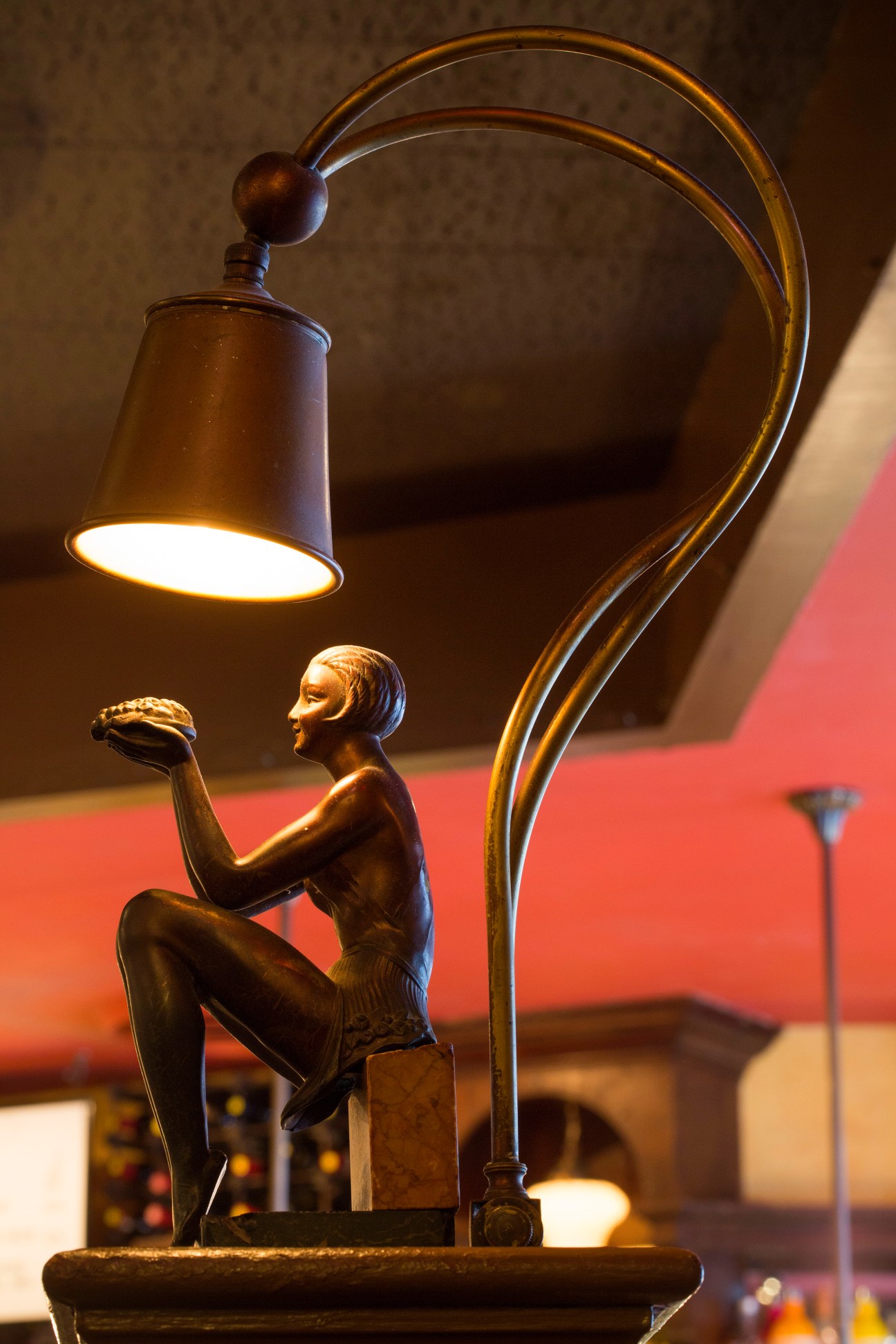 Bronze sculpture of a figure holding a hamburger beneath an arched lamp.
