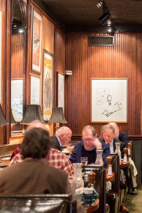 The wood-panelled interior of The Knickerbocker restaurant with diners seated at tables and framed artwork on the walls.
