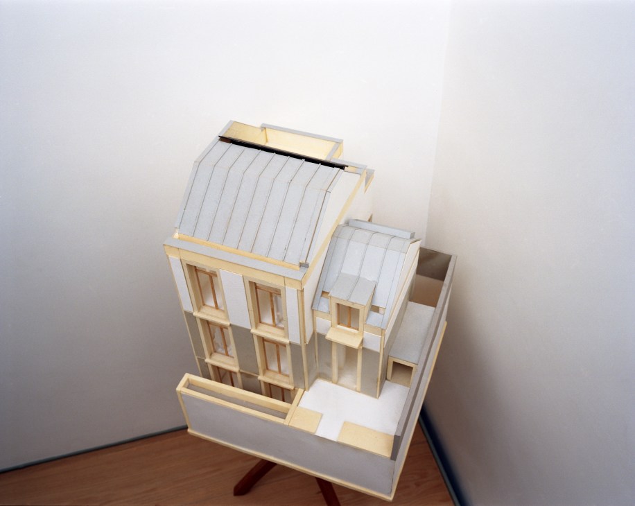 Architectural model of the Rational House showing a narrow townhouse design with light wood and white materials, featuring multiple windows and pitched roofs.