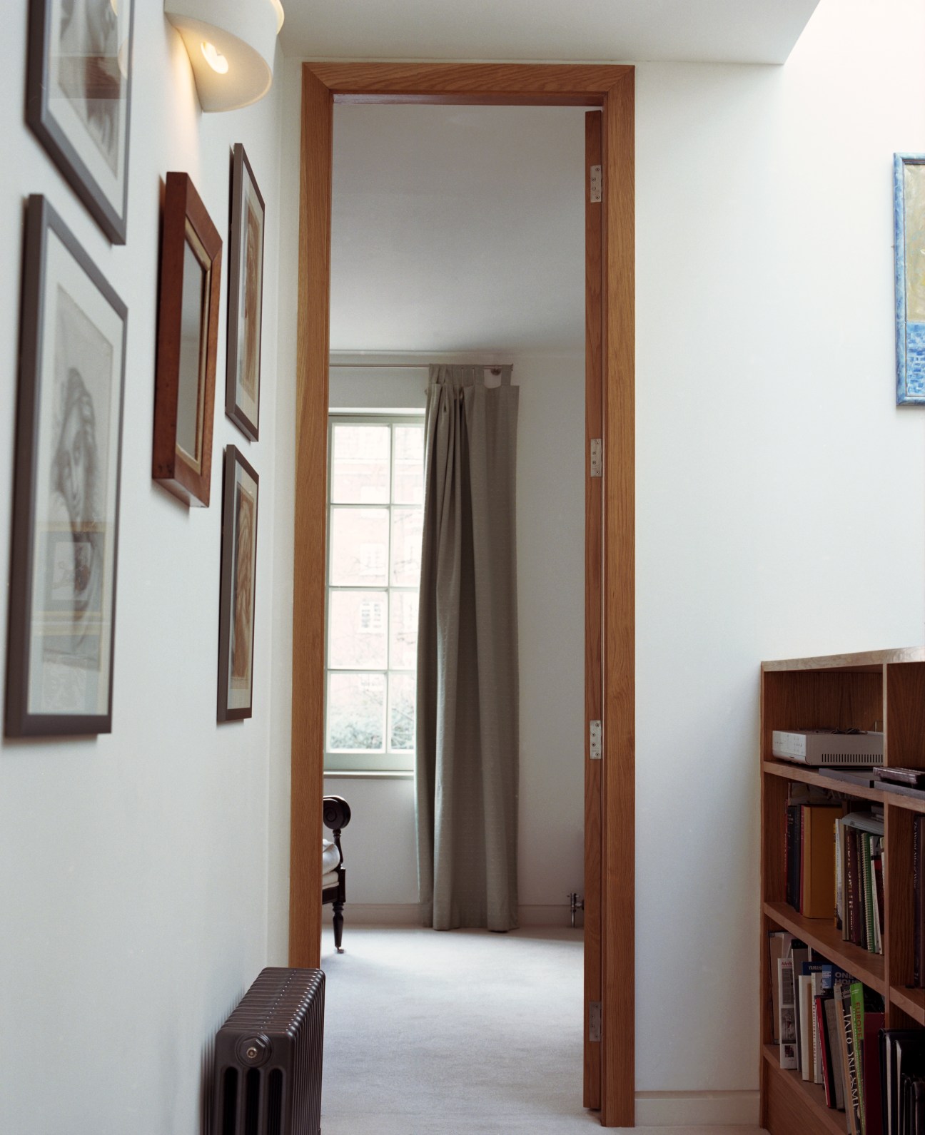 Interior hallway with tall wooden doorframe creating sense of height and space, white walls, and artwork.