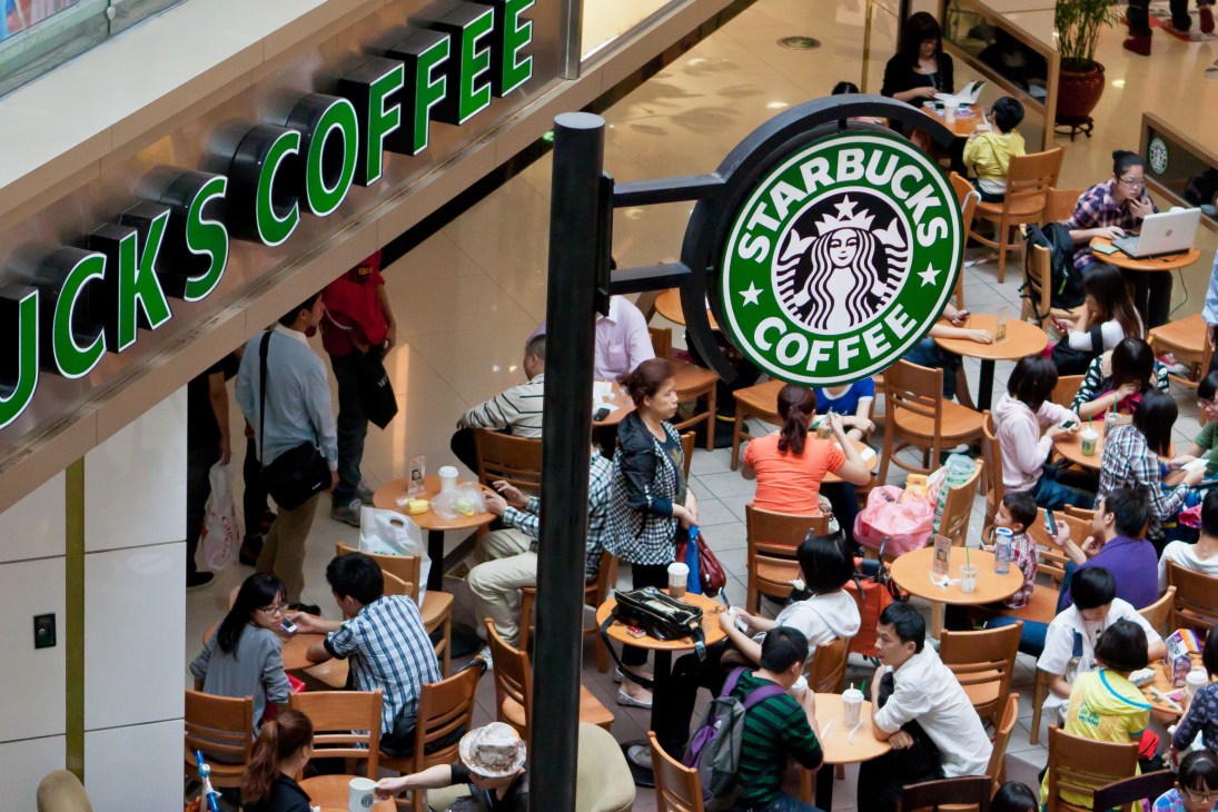 Overhead view of a busy Starbucks coffee shop with customers seated at tables in a shopping mall.